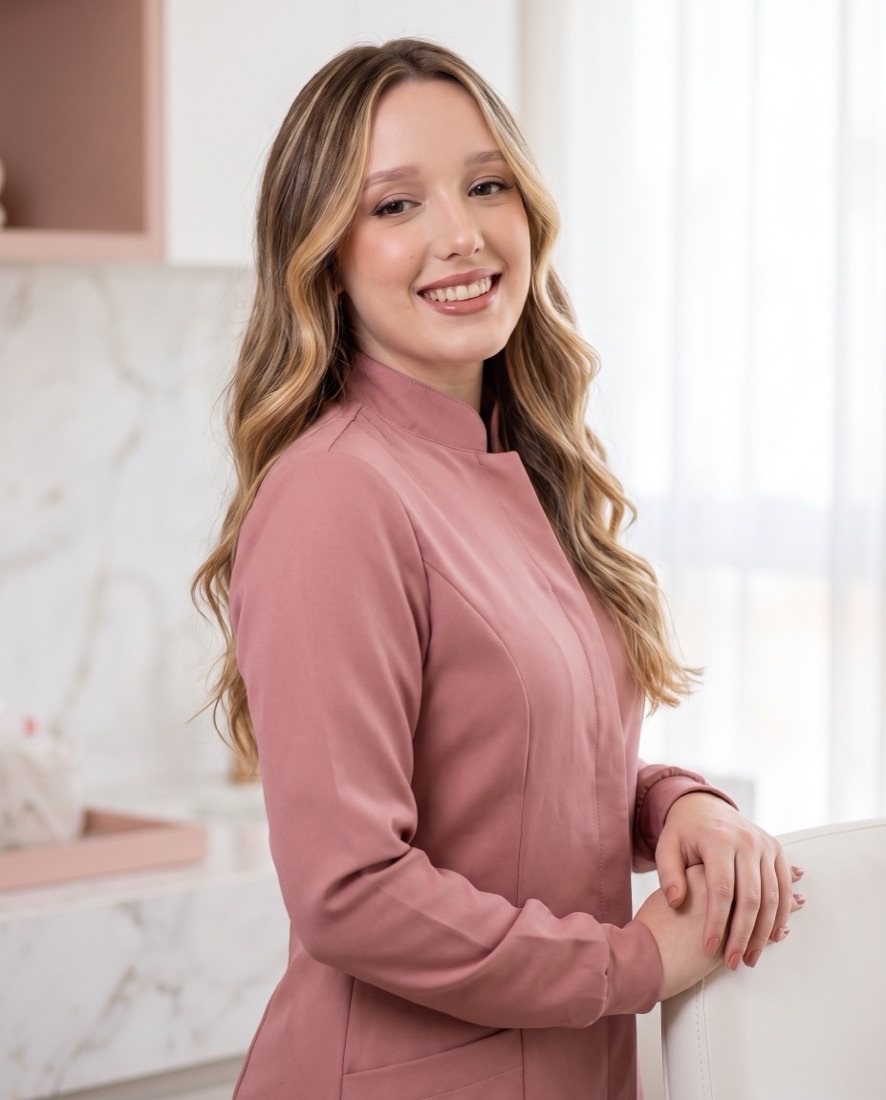 Dra. Gabriela Bobato de jaleco rosa no consultório