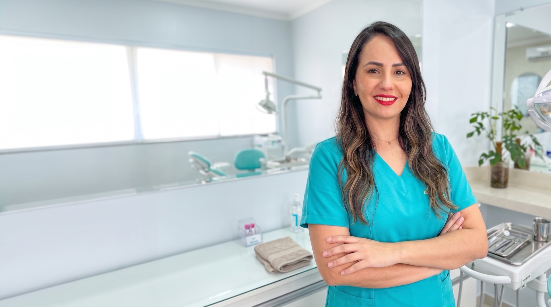 Dra. Romina Petrucci, de uniforme turquesa e braços cruzados, no consultório